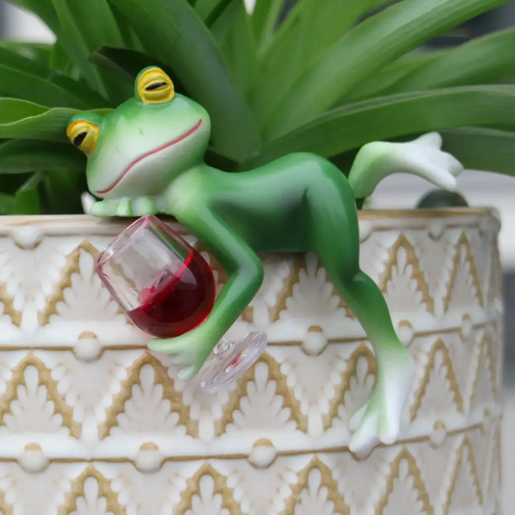 Resin frog decor figurine lounging on a patterned plant pot edge with a wine glass