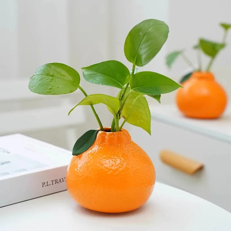 ceramic orange vase with greenery on tabletop near book