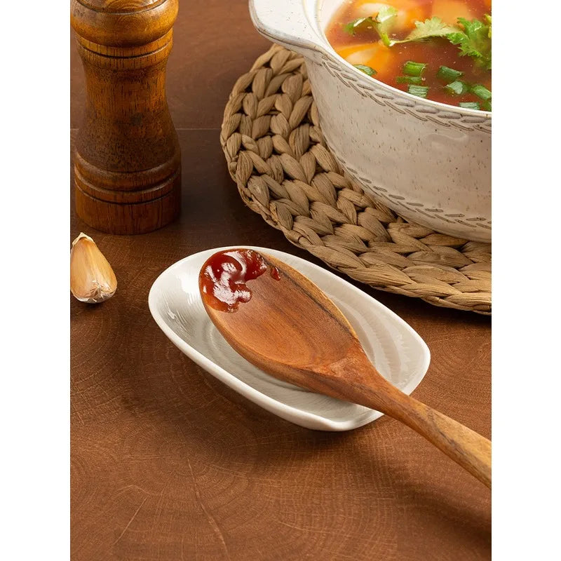 White ceramic spoon rest in use with a wooden spoon with sauce next to a pot of soup