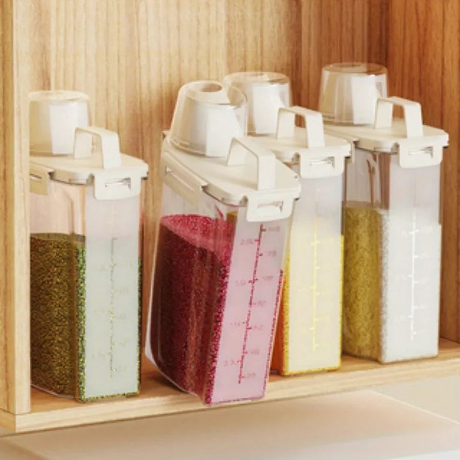 Four clear food storage bins with white lids and handles, each filled with different grains or dry foods, organized in a wooden pantry