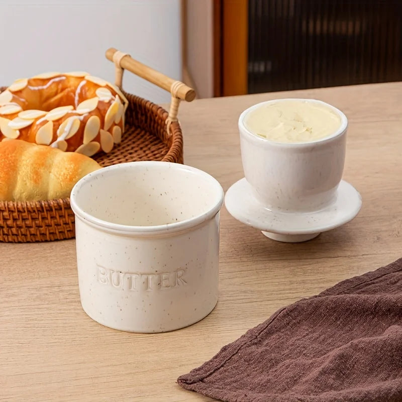 Speckled ceramic butter crock and lid set near bread basket on kitchen table