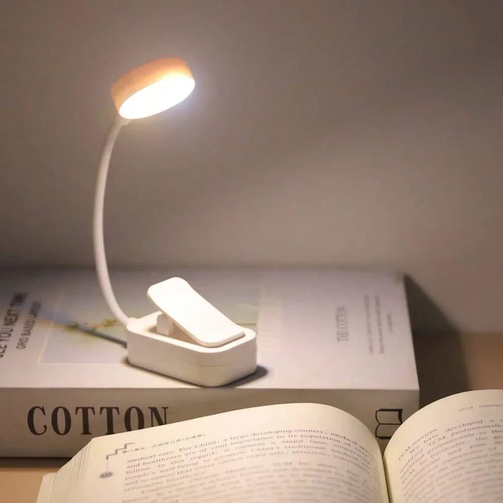 Mini LED clip-on book light illuminating a book on a bedside table