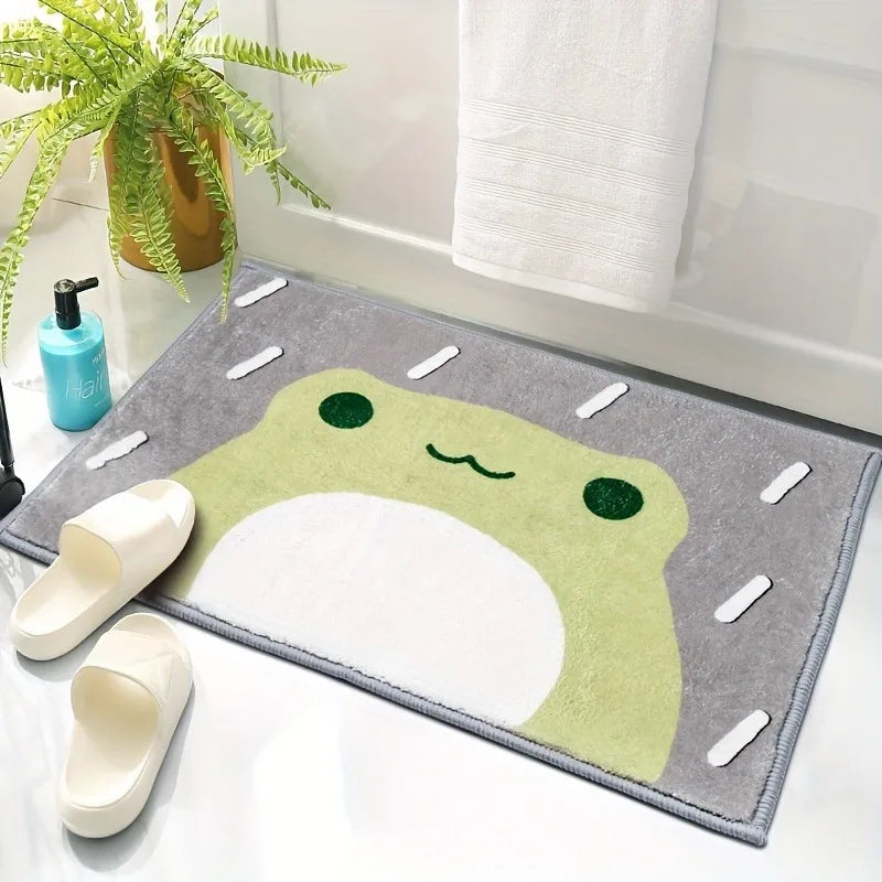 Soft frog bath mat in green and gray beside slippers and a plant in a bathroom