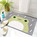 Soft frog bath mat in green and gray beside slippers and a plant in a bathroom