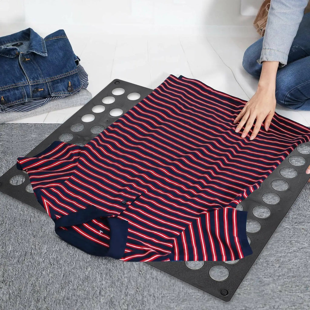 A person folding a striped shirt on a black folding laundry board with folded clothes on the side