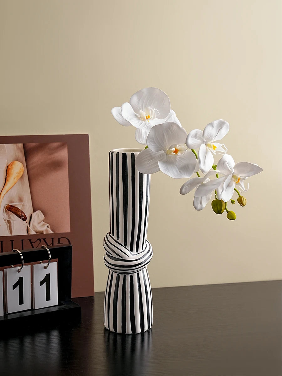 Tall black and white striped ceramic knot vase holding white orchid stems, styled on a modern tabletop.