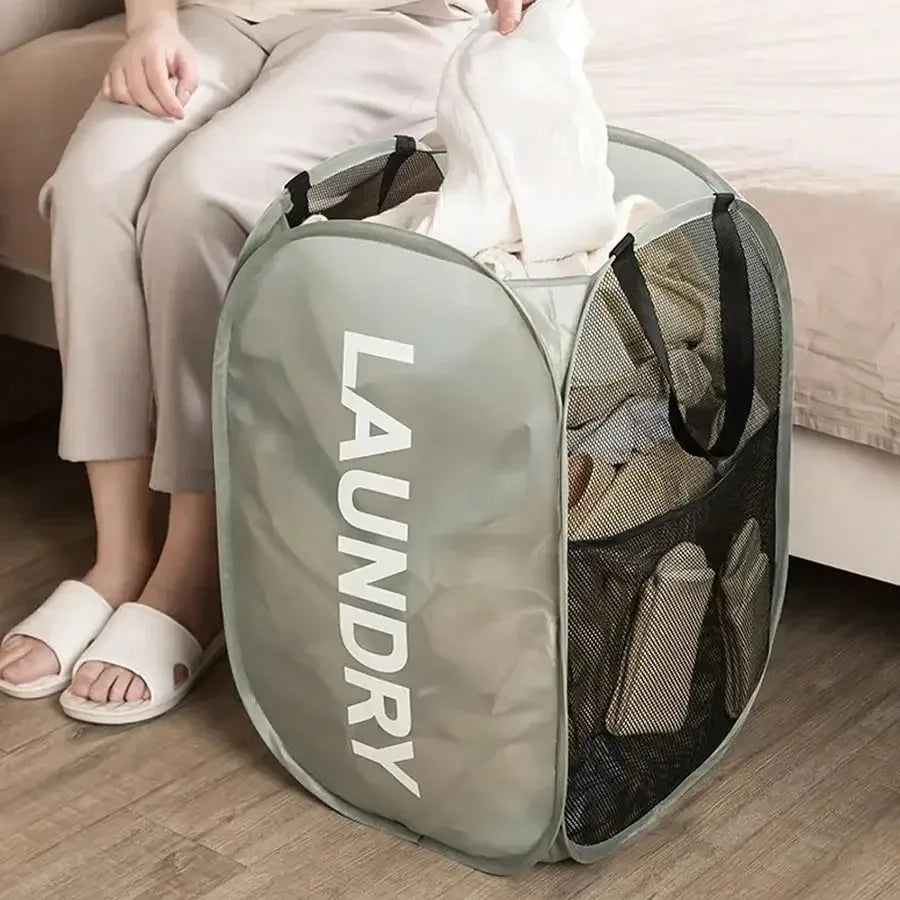 gray pop-up laundry hamper with large 'LAUNDRY' text beside a bed