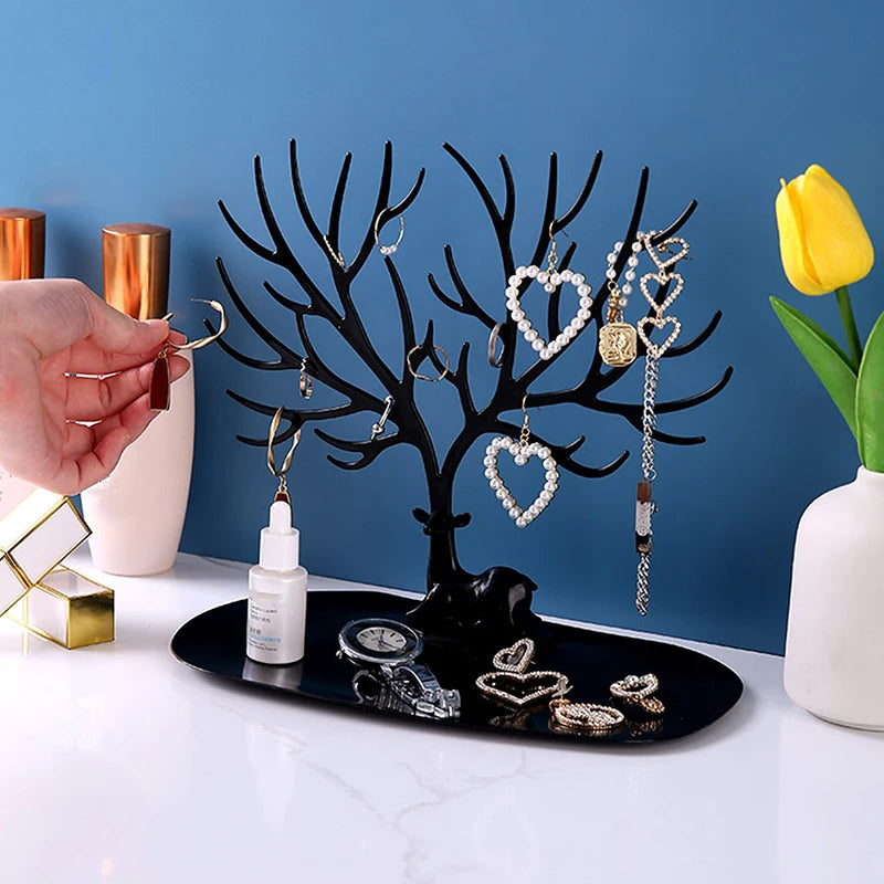 Black jewelry tree stand on a vanity, with a hand placing earrings and jewelry in place