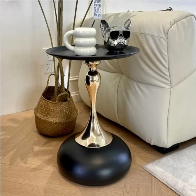 Modern black and gold metal side table beside a sofa, holding a mug and a decorative object