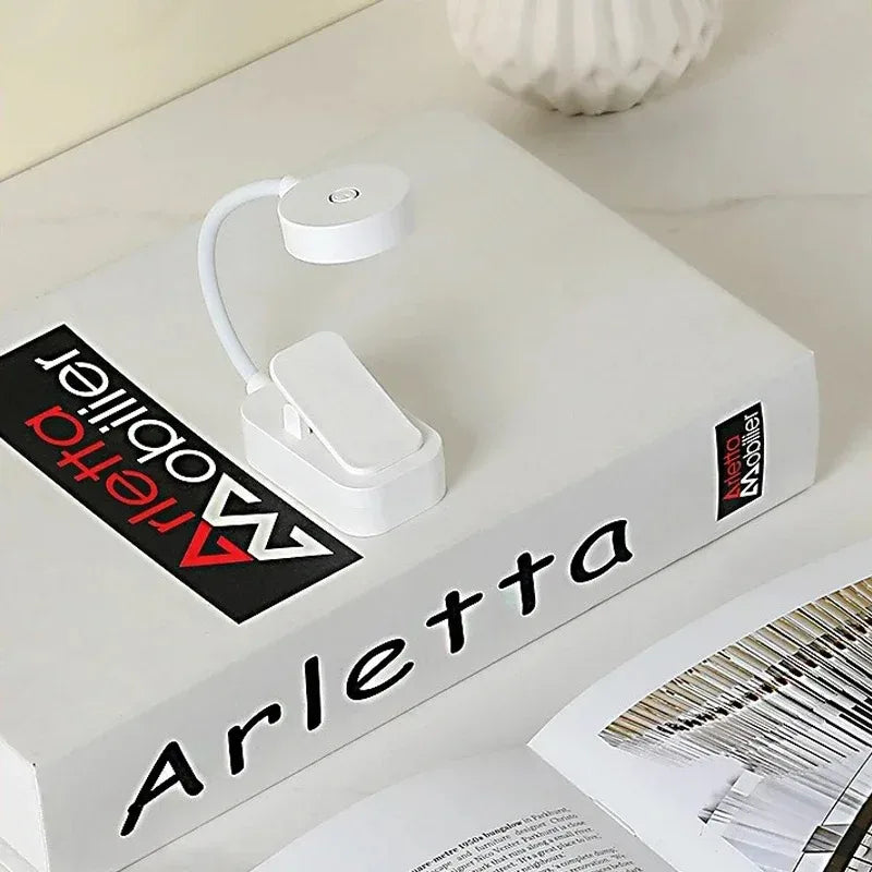 Compact white LED book lamp clipped onto hardcover book, on a light colored surface