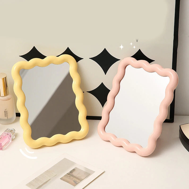 Yellow and pink wavy frame desktop mirrors beside beauty products.