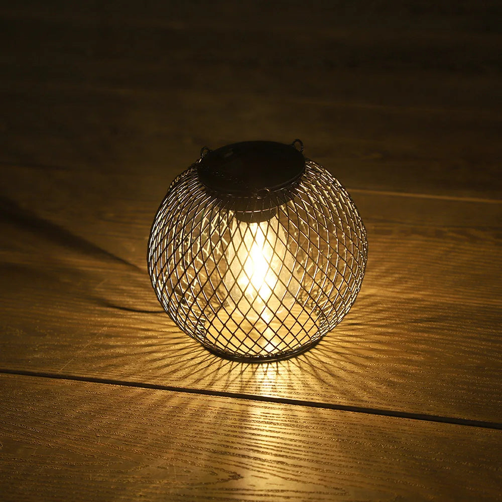 Black mesh outdoor solar lantern lit on a wooden surface in the evening