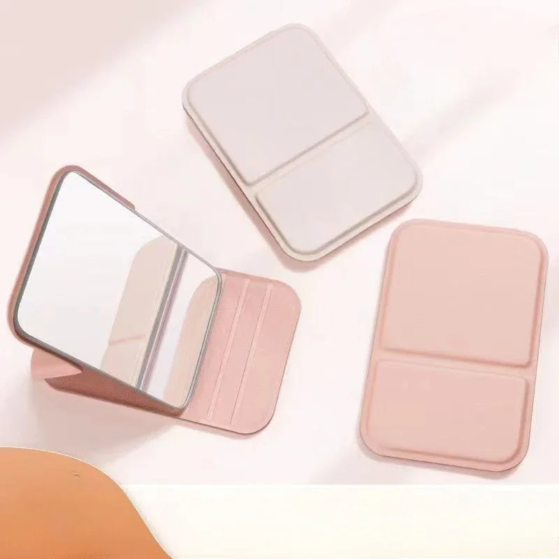 Overhead view of beige and pink foldable makeup mirrors, both open and closed, on a pink surface