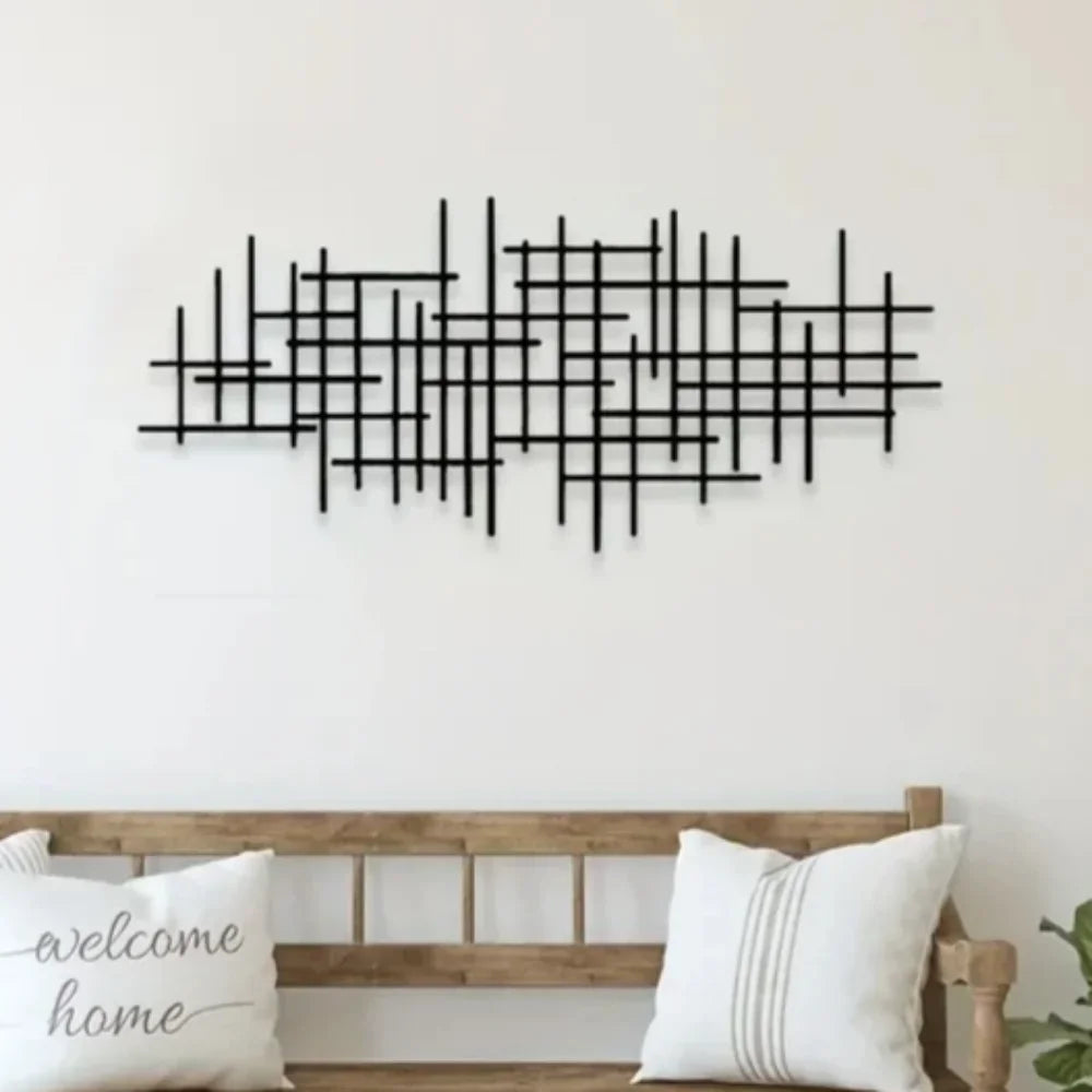Black abstract grid metal wall art sculpture displayed above a wooden entryway bench with white cushions