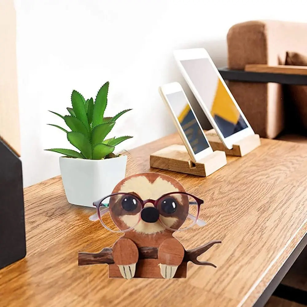 Sloth animal eyeglasses holder on a desk next to a plant and digital devices