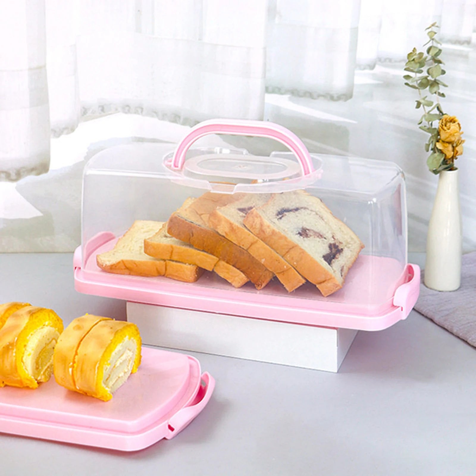 Rectangular bread box with clear lid displaying slices of bread and cake rolls in a bright kitchen