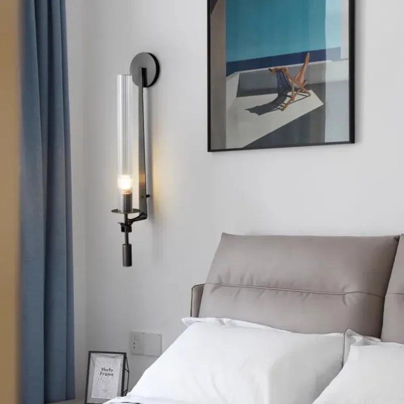black vertical wall sconce with clear ribbed shade above a pillow in bedroom