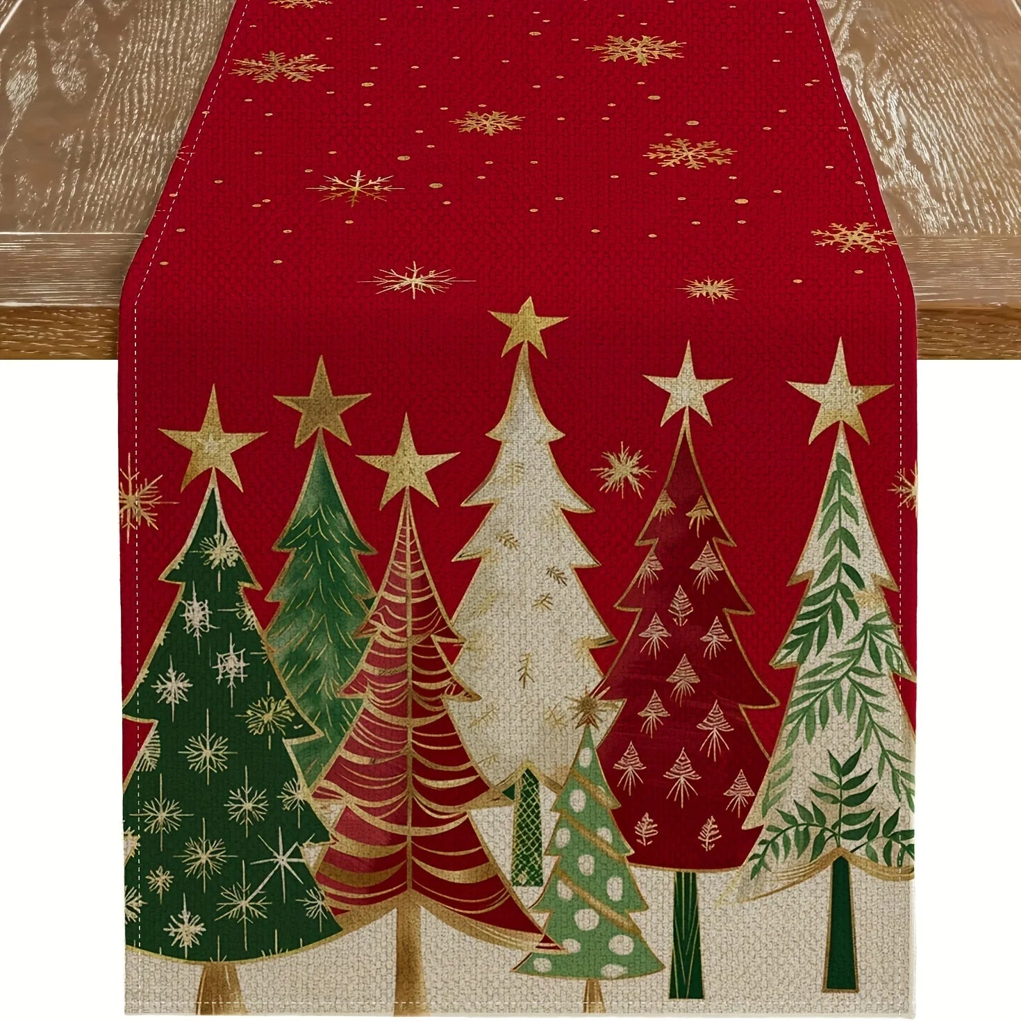 Red Christmas table runner with multicolor evergreen tree and gold star pattern draped on a wooden table
