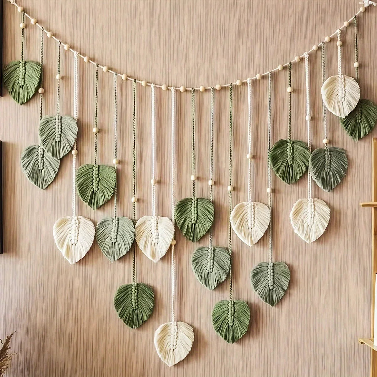 green and ivory woven leaf garland with wooden beads hung on a beige wall