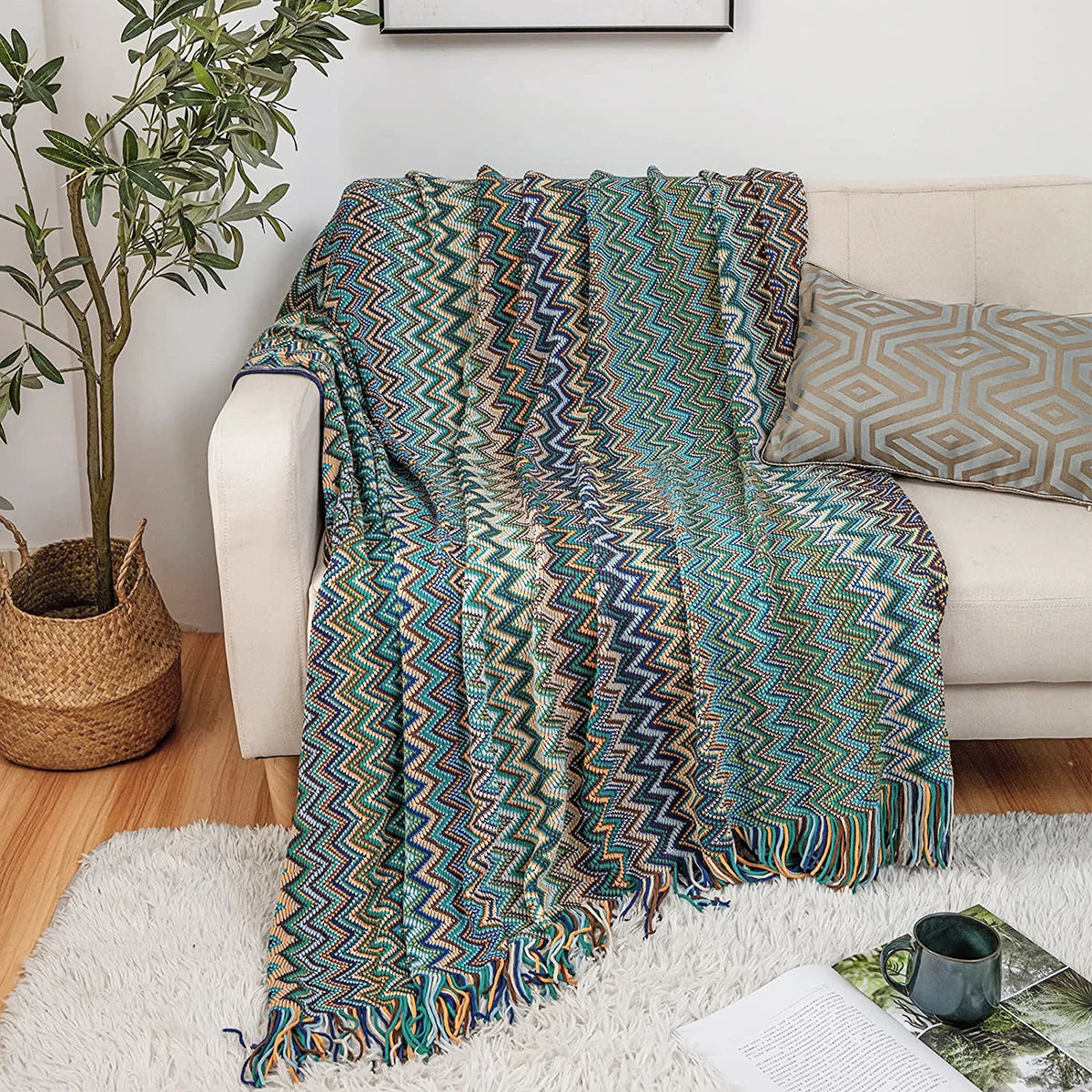 Blue and green zigzag patterned knit throw blanket with tassels laid across a sofa, styled with a geometric pillow