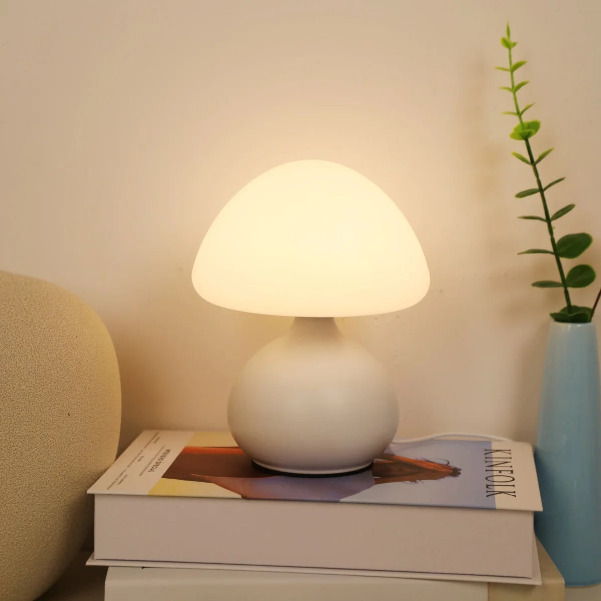 Softly lit white mushroom table lamp placed on stacked books with a vase nearby