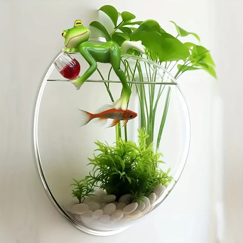 Frog figurine lounging on a glass wall planter with green plants and a goldfish inside.