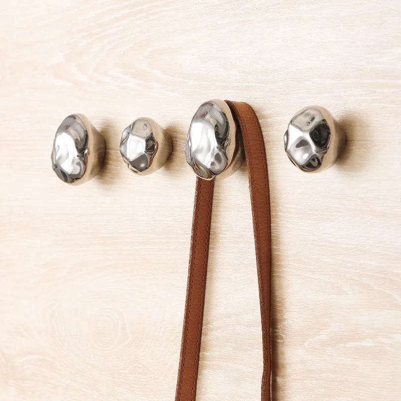 Four hammered silver stone wall hooks installed on wood wall, one holding a brown strap