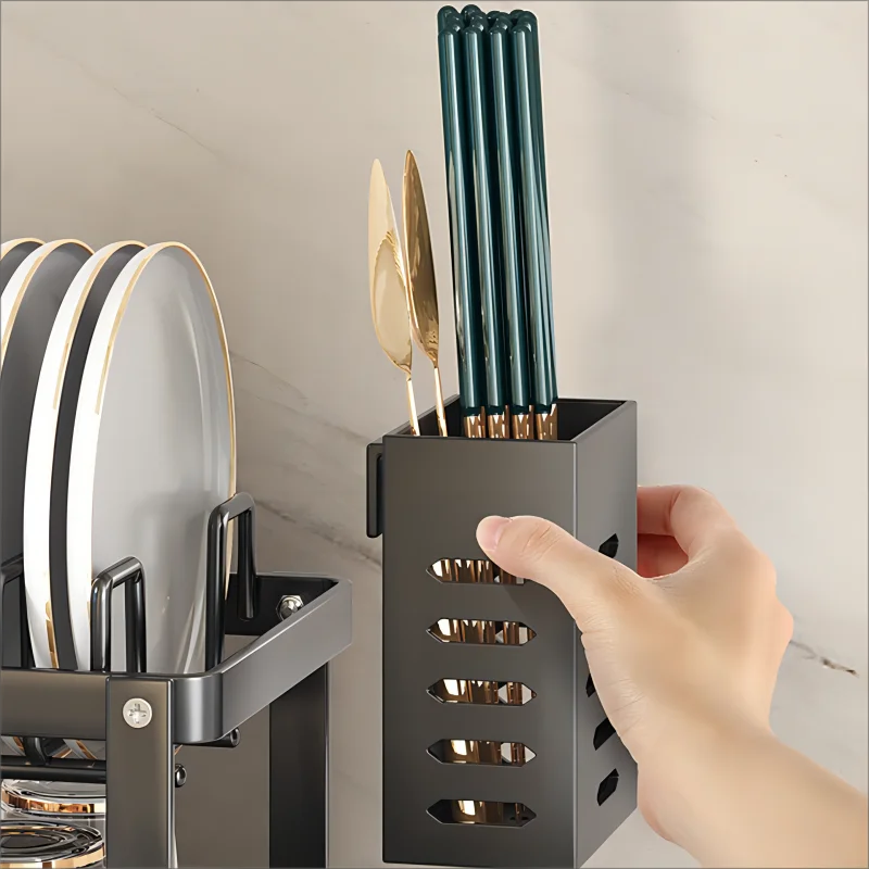 Removable black utensil holder being lifted from side of dish drying rack, with gold and green chopsticks inside