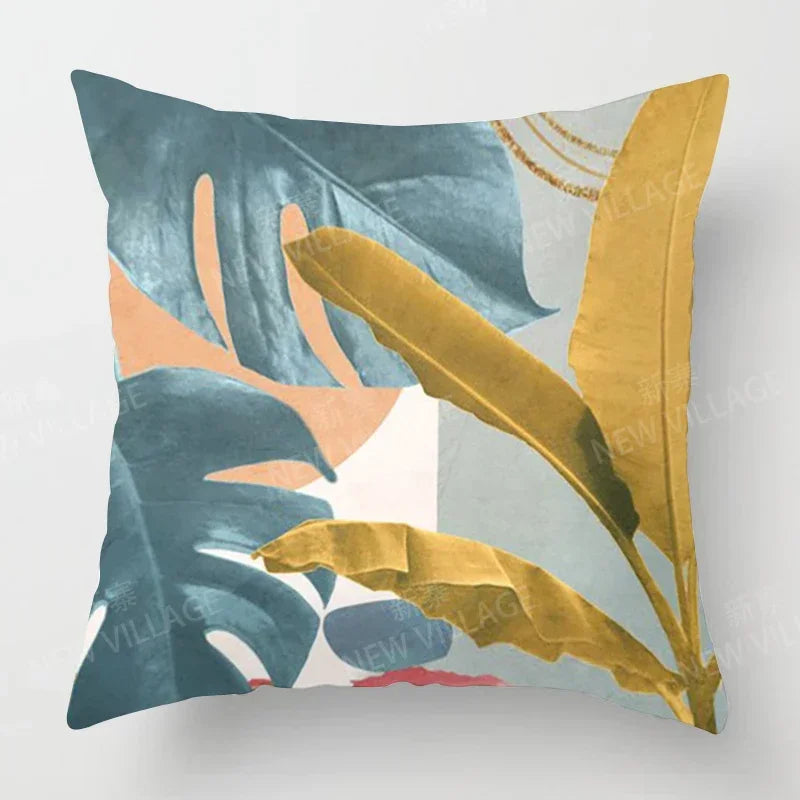 Close-up of a square throw pillow cover with large blue and yellow botanical leaves on a white and peach background.