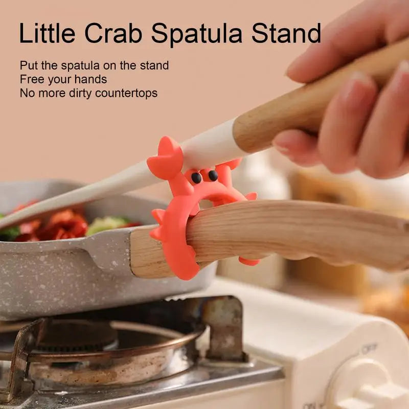 Crab-shaped silicone utensil rest holding a spatula on a wooden pot handle above a stovetop