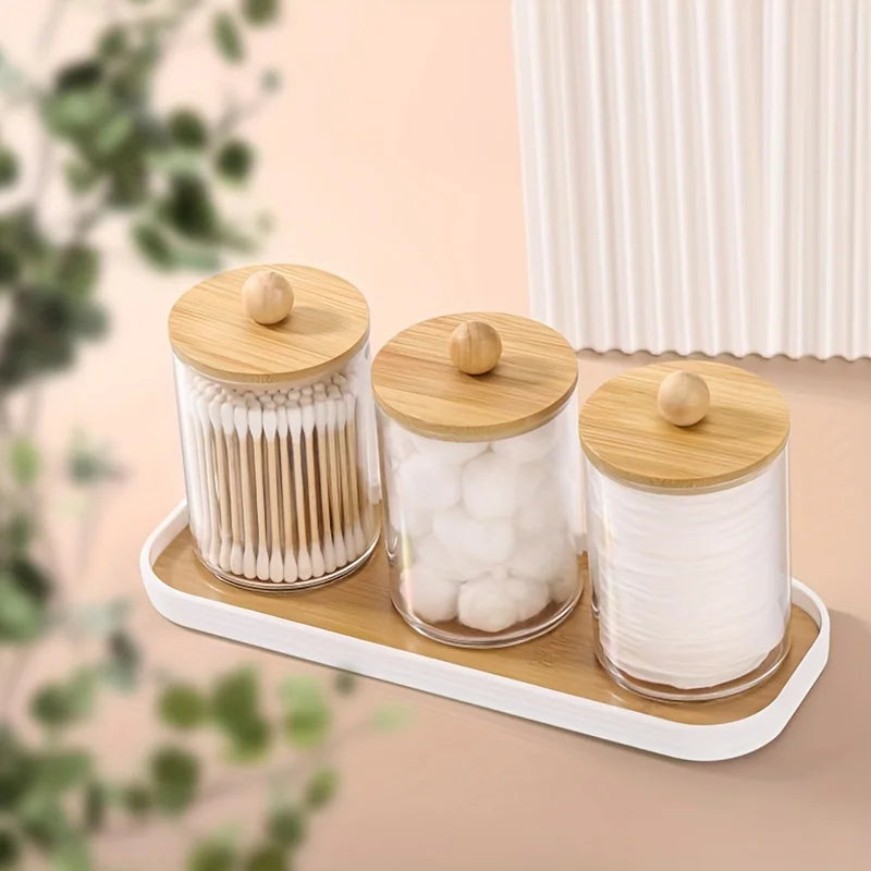 White-trimmed vanity tray with three glass jars for bathroom storage, styled on a peach surface