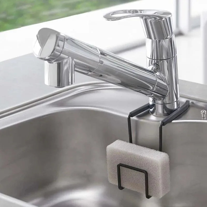 Black metal sponge holder hanging on a kitchen faucet with a white sponge