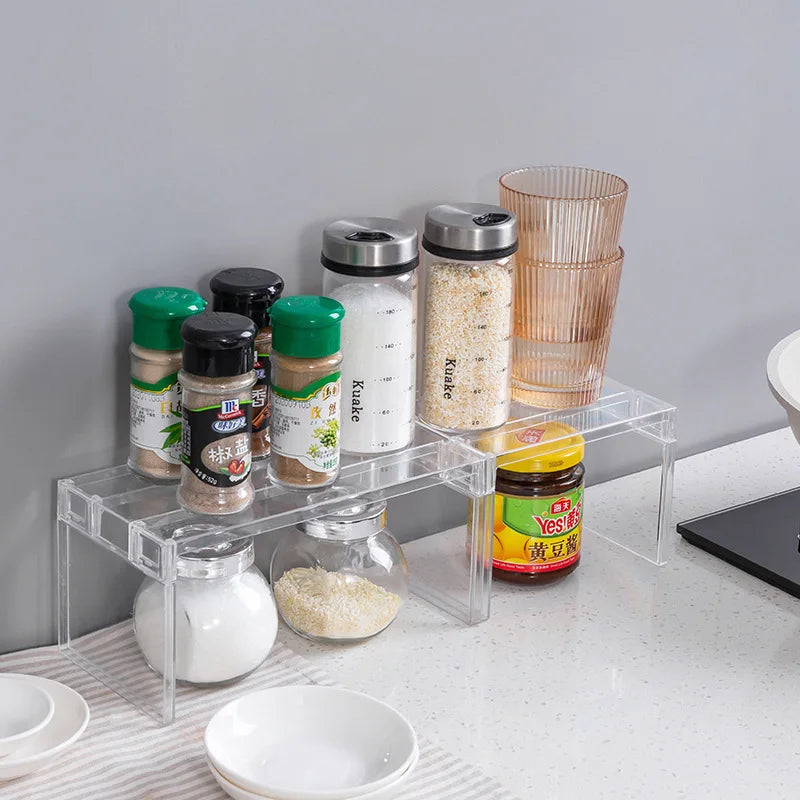 Clear plastic shelf riser organizing spice jars and glasses on a kitchen countertop