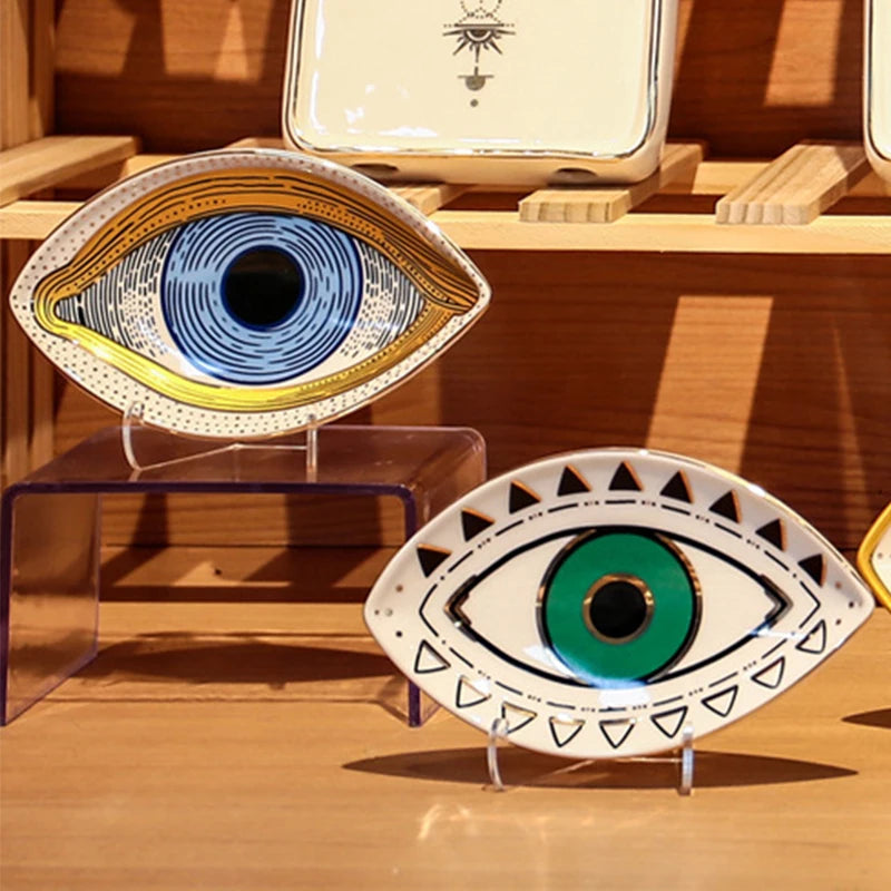 Two eye-shaped ceramic trinket trays with colorful designs, displayed on a shelf