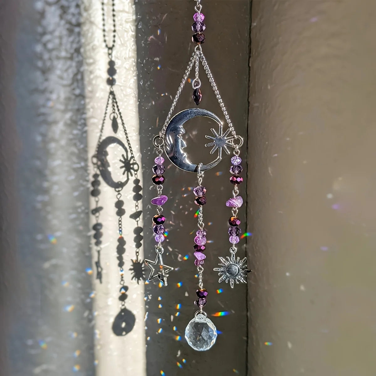 Silver celestial moon and sun crystal suncatcher hanging in a window, reflecting rainbow light and casting shadows.