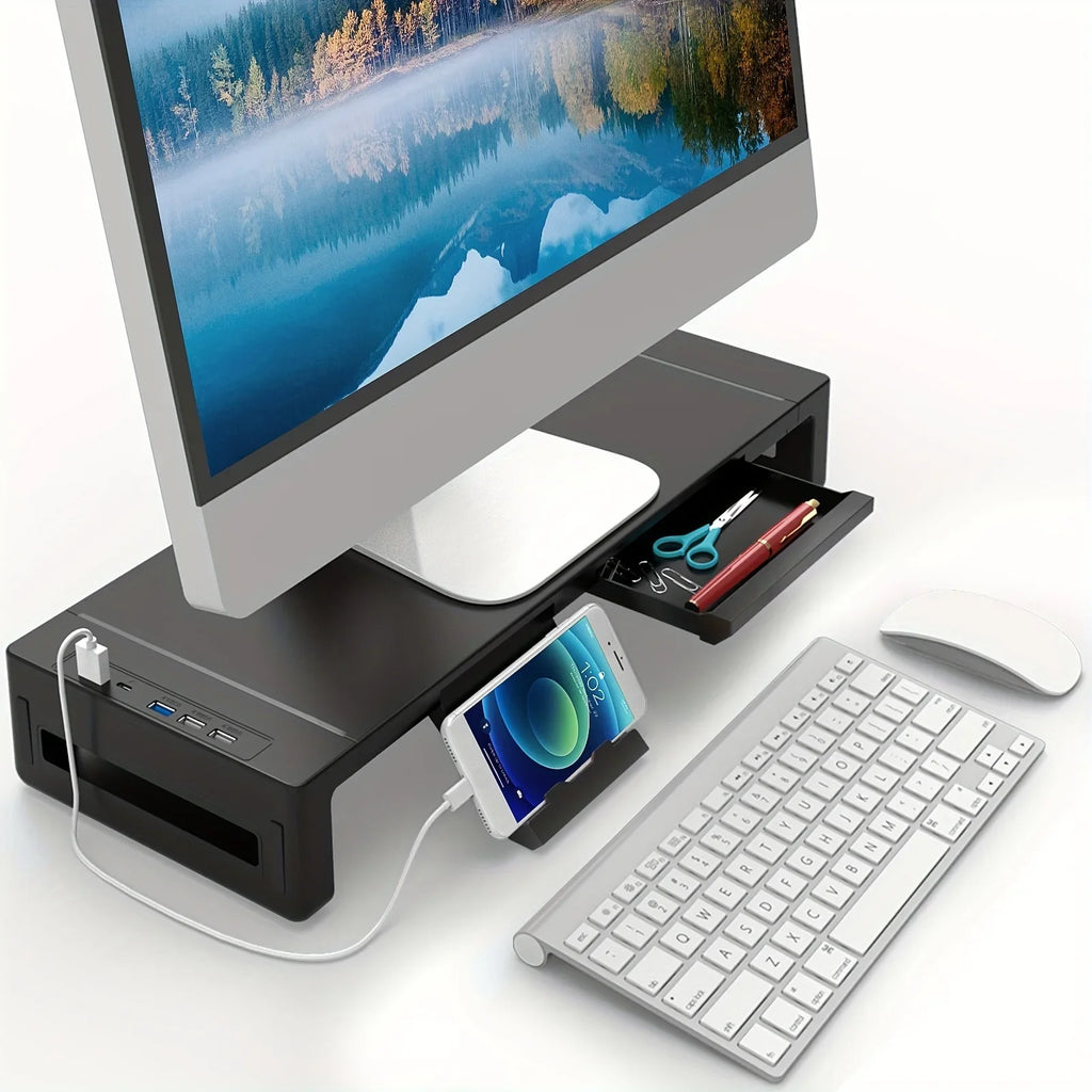 Black adjustable monitor riser with drawer, USB ports, and phone stand in use on a desk with keyboard and mouse