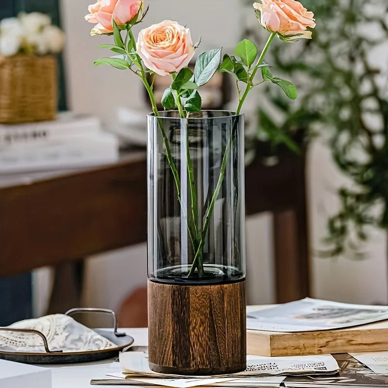 Smoked glass vase with wooden base holding pink roses on a table in a cozy living room