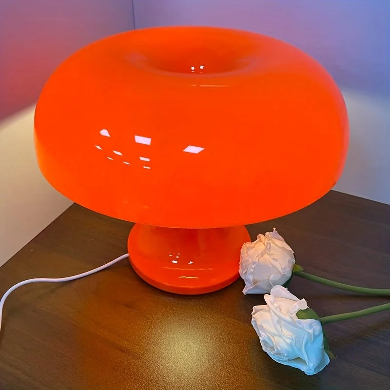 Fluorescent orange mushroom-shaped table lamp on dark wood surface with white flowers