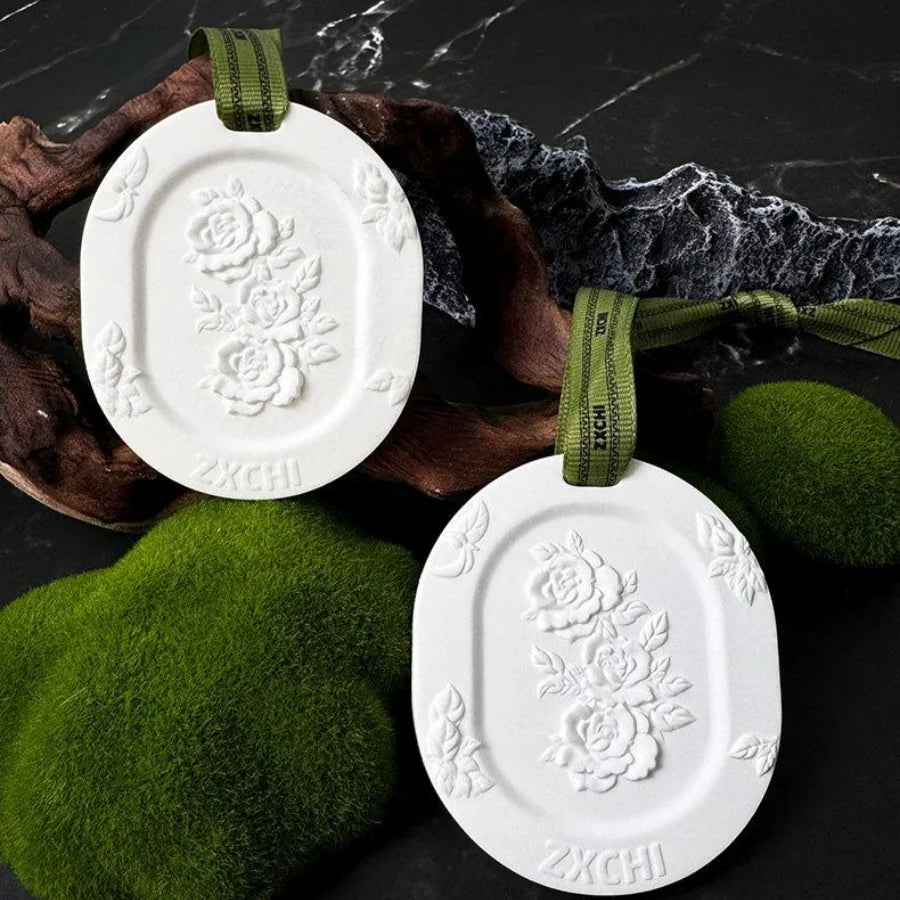 Two white floral embossed hanging gypsum stones with green ribbons on a dark natural background