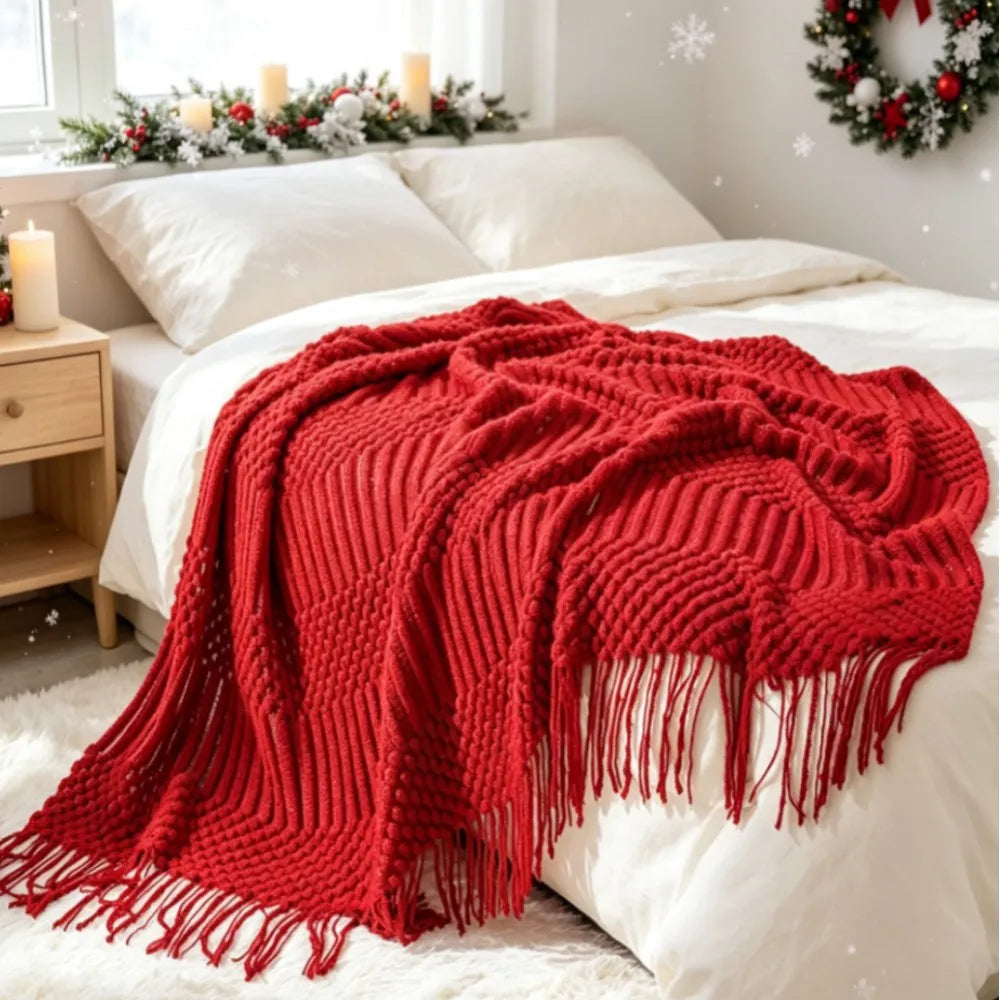Red knit throw blanket with tassels draped over a bed in a cozy white bedroom with holiday decor