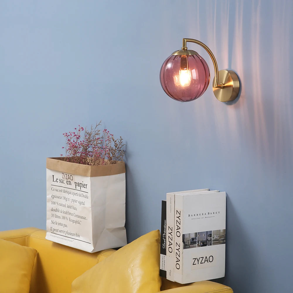 Rose red glass globe wall sconce with brass arm on blue wall above a yellow sofa