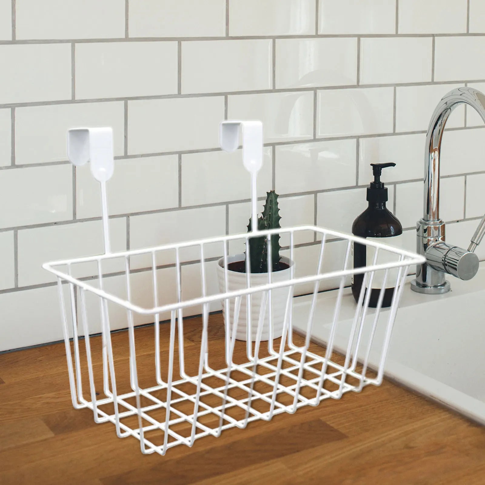 White over-the-cabinet metal basket organizer hanging on cabinet door beside kitchen sink