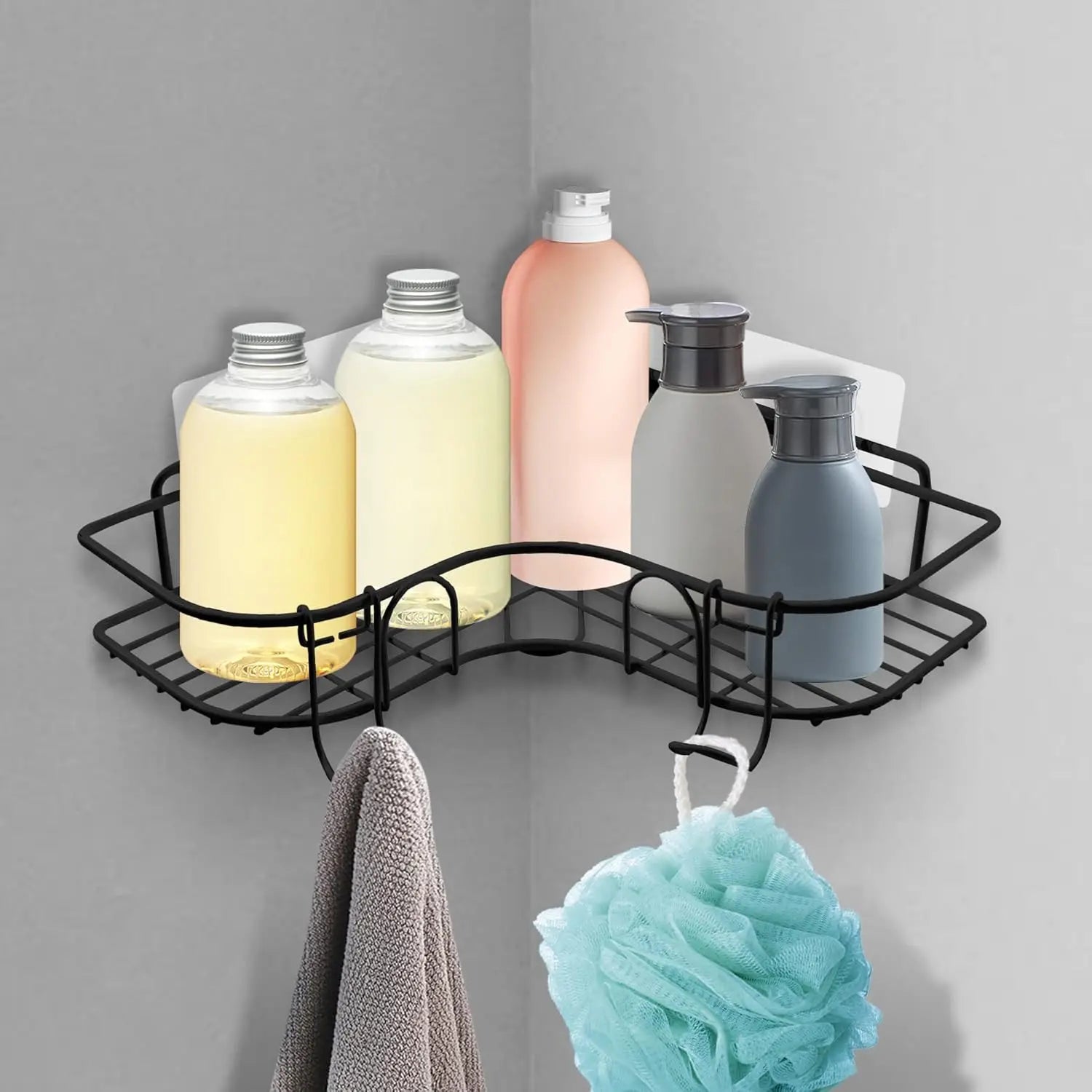 Black metal wall-mounted corner shelf installed in a bathroom, holding bottles and showing removable hooks with a towel and shower pouf