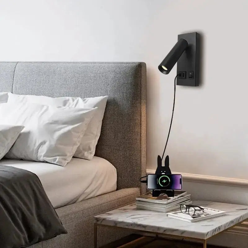 Black wall-mounted reading light with USB port, shown in use above a bedroom nightstand