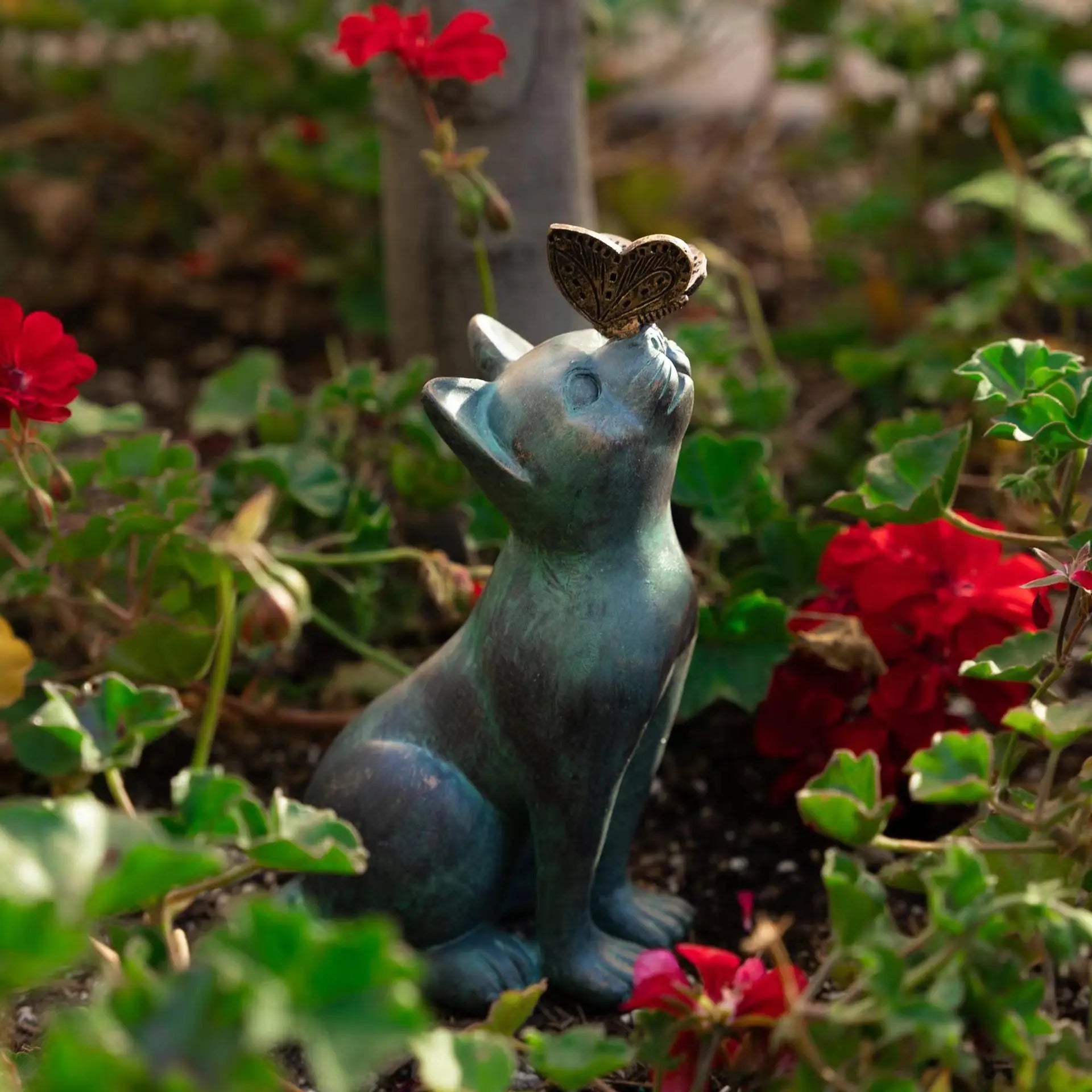 Cat and butterfly garden statue surrounded by blooming flowers outdoors