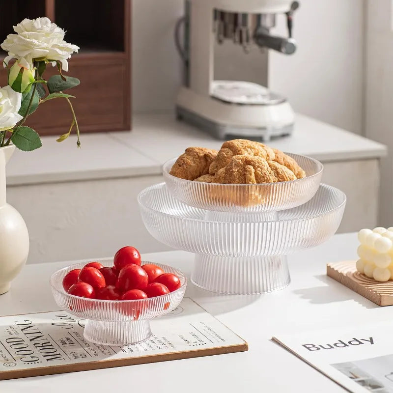 Two ribbed glass pedestal bowls on a kitchen counter, one with tomatoes and one with pastries
