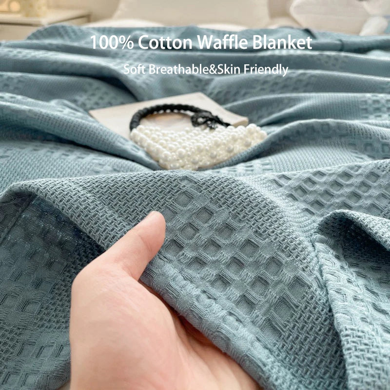 Hand touching soft blue cotton waffle throw blanket on bed