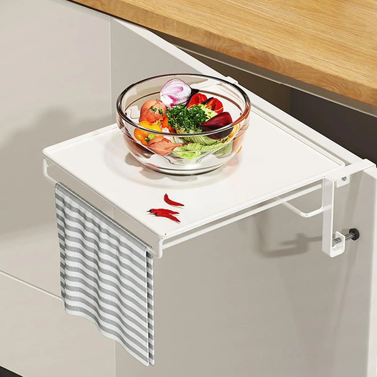 White foldable over-cabinet shelf with towel bar in use on a kitchen cabinet, holding a bowl of vegetables and a striped towel
