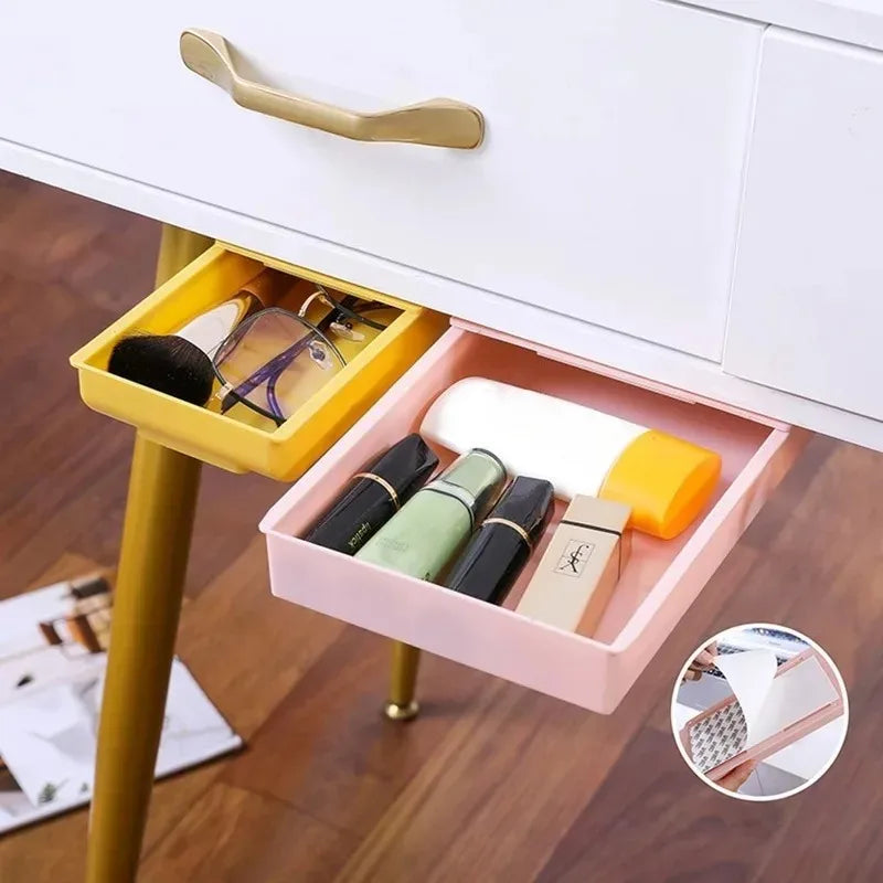 Yellow and pink under-desk storage drawers holding makeup and glasses, shown attached under vanity table with close-up of adhesive strip