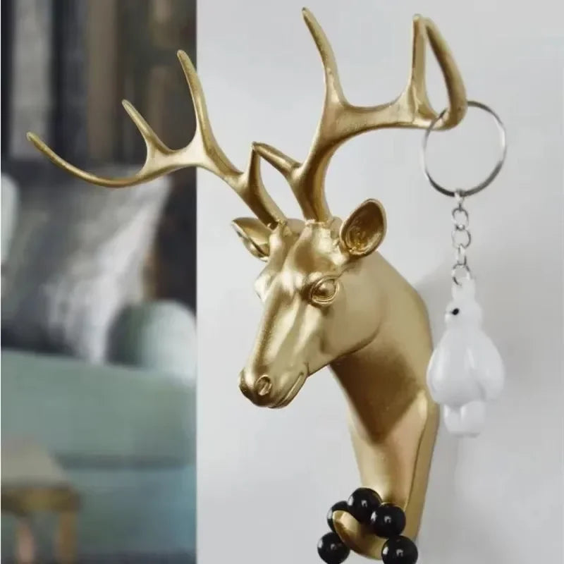 Gold deer head wall hook holding a keychain and beaded bracelet in a home entryway setting